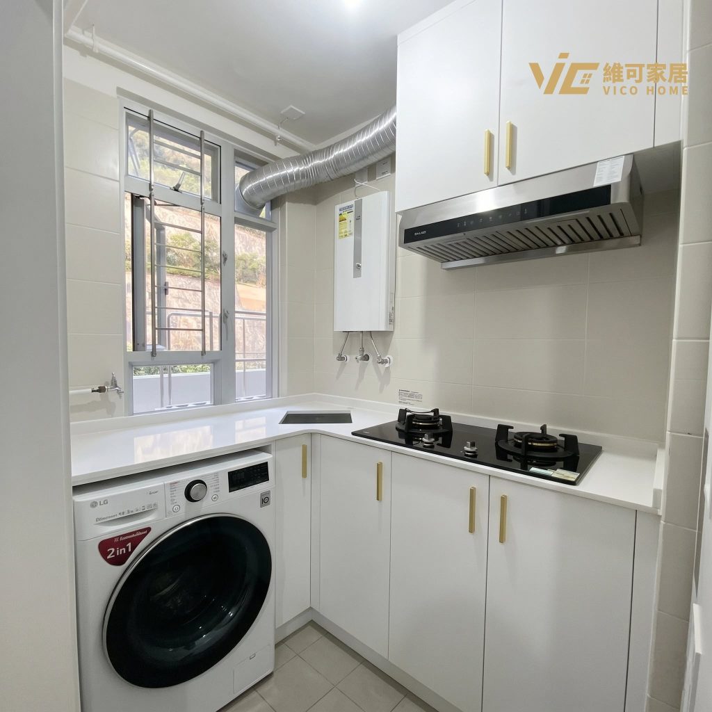 hk-custom-kitchen-service 20 白色廚櫃配石英檯面,L 型佈局,金色把手,洗衣機與爐具內嵌,窗外見綠樹。