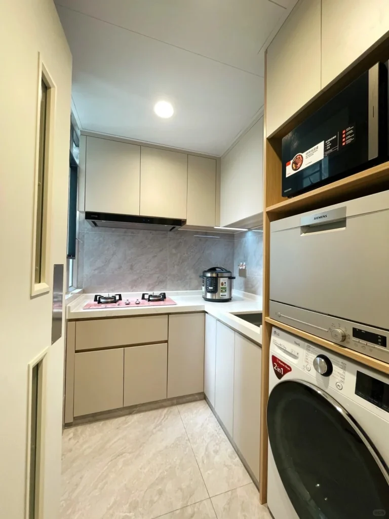 hk-custom-kitchen-service 11 米白色無手把廚櫃配大理石紋檯面,L 型佈局,微波爐、洗衣機及電飯煲內嵌,窗外有景。