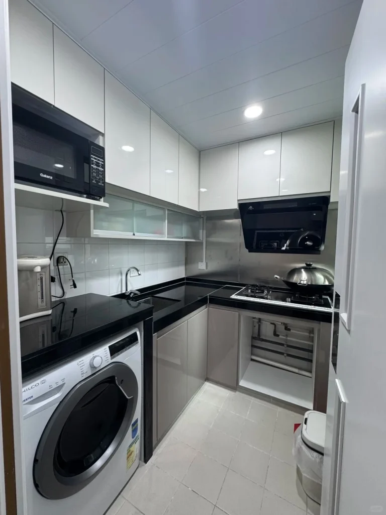 hk-custom-kitchen-service 7 白色無手把廚櫃配黑色石英檯面,L 型佈局,微波爐、洗衣機及抽油煙機內嵌。